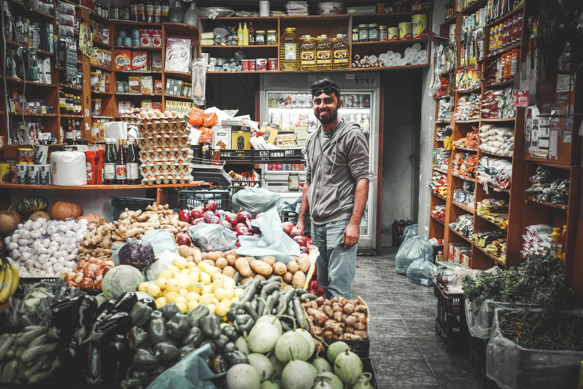 A grocer standing among crates of fresh produce and packed shelves